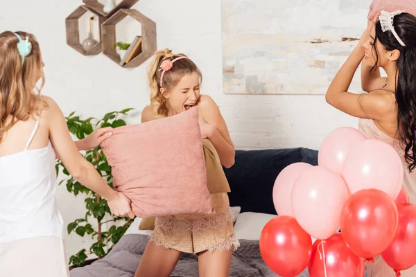 Belles filles multiethniques s'amuser et se battre avec des oreillers pendant la soirée pyjama dans la chambre — Photo de stock