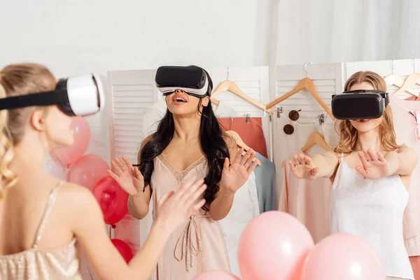 Chicas multiétnicas en ropa de dormir y auriculares vr que tienen experiencia de realidad virtual durante la fiesta de pijama - foto de stock