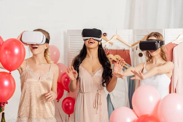 Chicas multiétnicas excitadas en ropa de dormir y auriculares vr que tienen experiencia de realidad virtual durante la fiesta de pijama - foto de stock