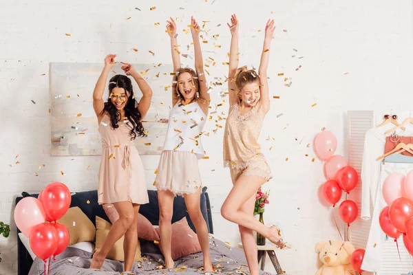 Beautiful multicultural girls in nightwear dancing and having fun under falling confetti during pajama party — Stock Photo