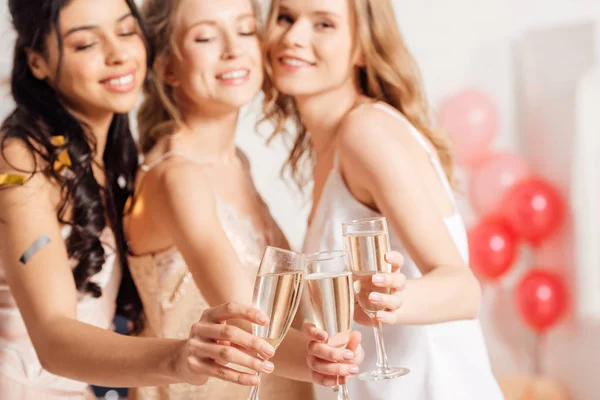 Selective focus of champagne glasses with beautiful smiling multicultural girls in nightwear on background — Stock Photo