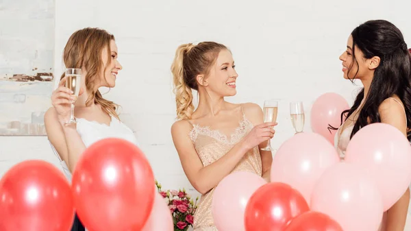 Schöne multikulturelle Mädchen in Nachtwäsche feiern mit Gläsern Champagner und Luftballons während Pyjama-Party — Stockfoto