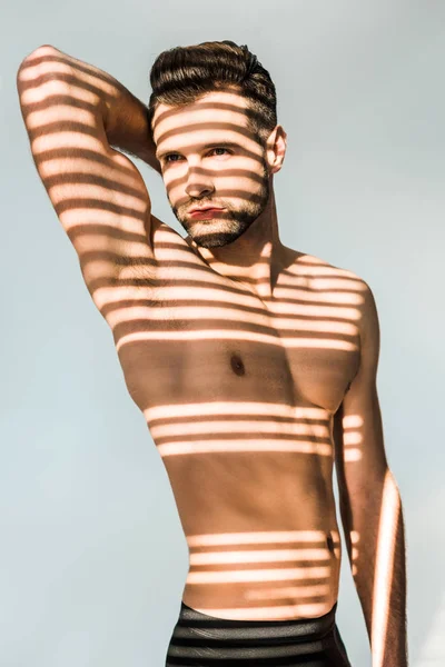 Handsome seductive man with shadows on muscular torso isolated on grey — Stock Photo