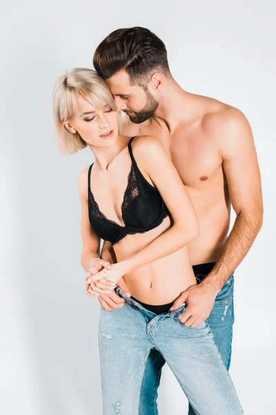 Красива чуттєва пара в нижній білизні і джинсах обіймається ізольовано на сірому — стокове фото