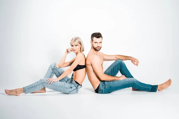 Beautiful girlfriend and handsome boyfriend in underwear and jeans sitting back to back on grey — Stock Photo