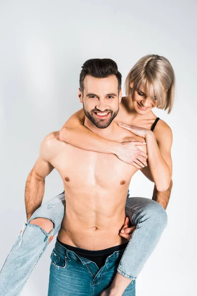 Smiling shirtless boyfriend piggybacking beautiful happy girlfriend isolated on grey — Stock Photo