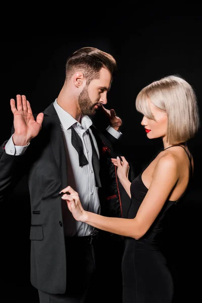 Elegant blonde woman undressing handsome man isolated on black — Stock Photo