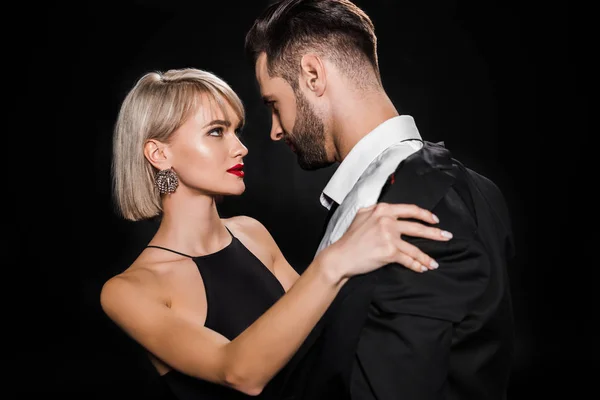 Leidenschaftliche blonde Frau zieht schönen Mann isoliert auf schwarz aus — Stockfoto