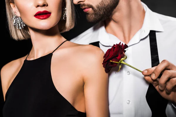 Cropped view of man touching womans shoulder with rose flower, isolated on black — Stock Photo