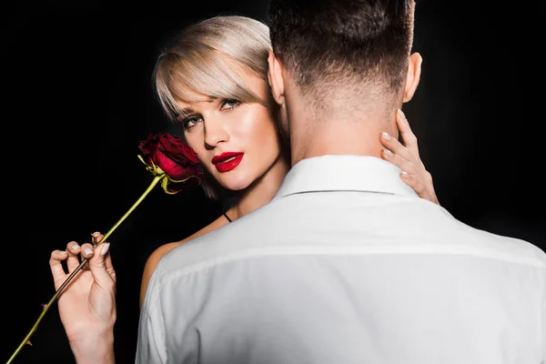 Sensual namorada segurando vermelho rosa flor enquanto abraçando namorado, isolado no preto — Fotografia de Stock