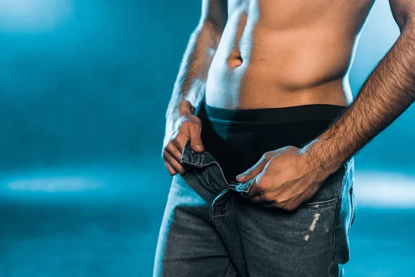 Cropped view of sexy man in black underwear and jeans posing on blue smoky background — Stock Photo