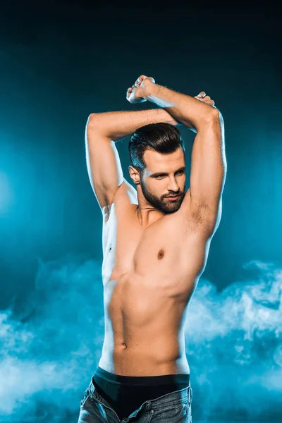 Handsome sexy man in black underwear and jeans posing on blue smoky background — Stock Photo
