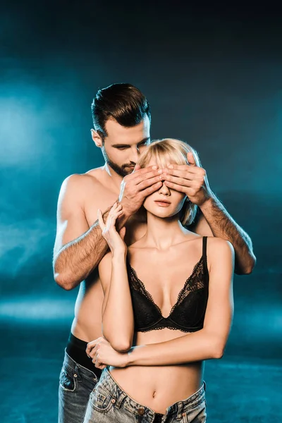 Handsome boyfriend closing eyes of blonde girlfriend on blue smoky background — Stock Photo