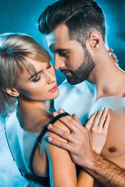 Handsome boyfriend undressing sensual girl on blue smoky background — Stock Photo