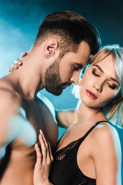 Tierna hermosa pareja con los ojos cerrados abrazando sobre fondo ahumado azul - foto de stock