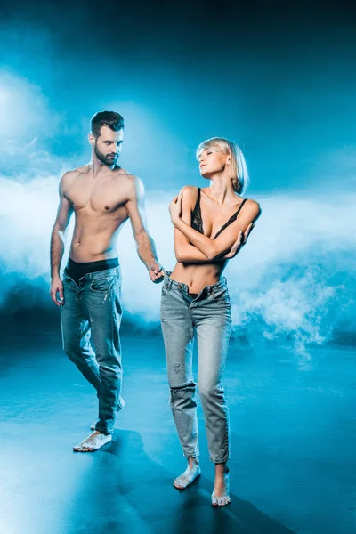 Beautiful couple in jeans and underwear on blue smoky background — Stock Photo