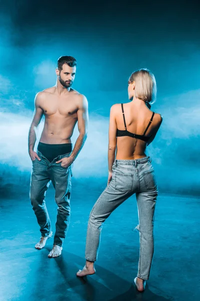 Beautiful couple in jeans and underwear posing on blue smoky background — Stock Photo