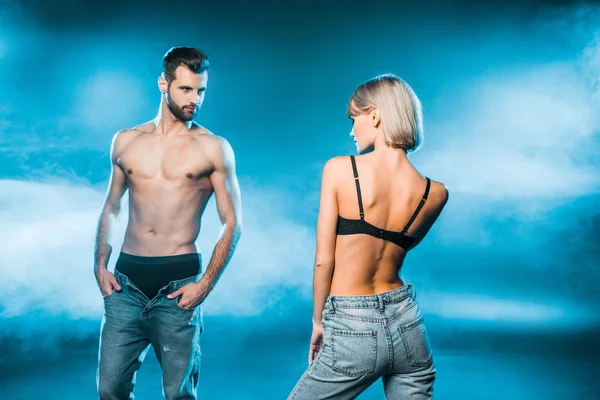 Casal sensual em jeans e roupa interior posando no fundo fumegante azul — Fotografia de Stock