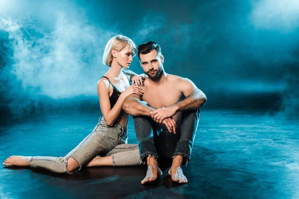 Beautiful sensual couple hugging and sitting on blue smoky background — Stock Photo