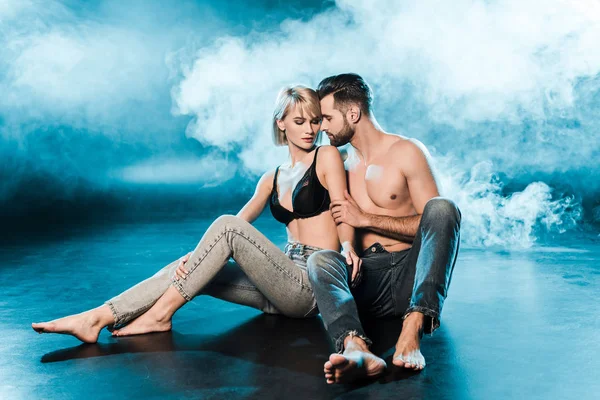 Seductive couple hugging and sitting on blue smoky background — Stock Photo