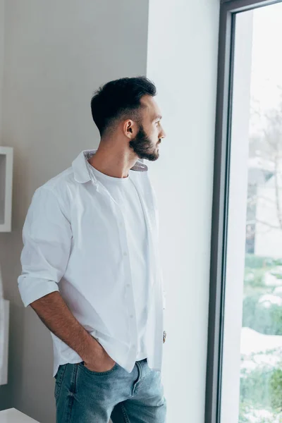 Pensive man standing with hand in pocket and looking at window — Stock Photo