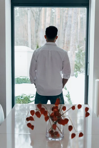 Вид сзади на брюнетку в белой рубашке, смотрящую в окно — стоковое фото