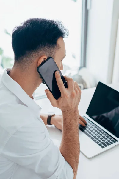 Brunette homme parlant sur smartphone et tapant sur le clavier de l'ordinateur portable — Photo de stock