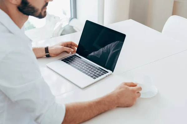 Чоловік у білій сорочці п'є каву та використовує ноутбук — стокове фото