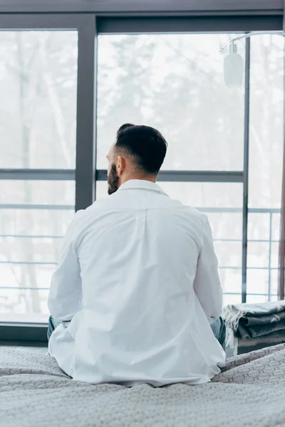 Vista trasera de hombre morena en camisa blanca sentado en la cama - foto de stock