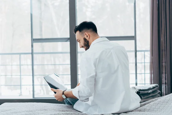 Веселий брюнетка людина з ноутбуком сидить на ліжку — стокове фото