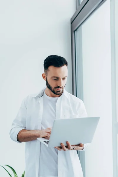 Концентрований красивий чоловік у білій сорочці тримає ноутбук — стокове фото