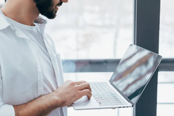 Vista cortada do homem barbudo na camisa branca segurando laptop — Fotografia de Stock