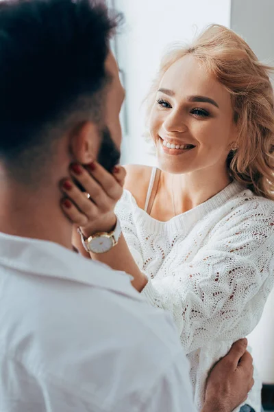 Menina sorridente em camisola de malha tocando suavemente o rosto do namorado — Fotografia de Stock