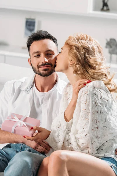 Menina loira segurando caixa presente e beijando namorado na bochecha — Fotografia de Stock