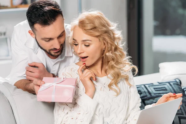 Handsome man presenting gift to surprised blonde woman — Stock Photo
