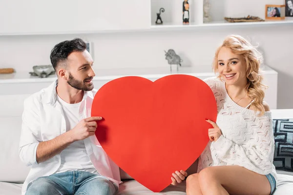 Smiling romantic couple holding big red heart — Stock Photo