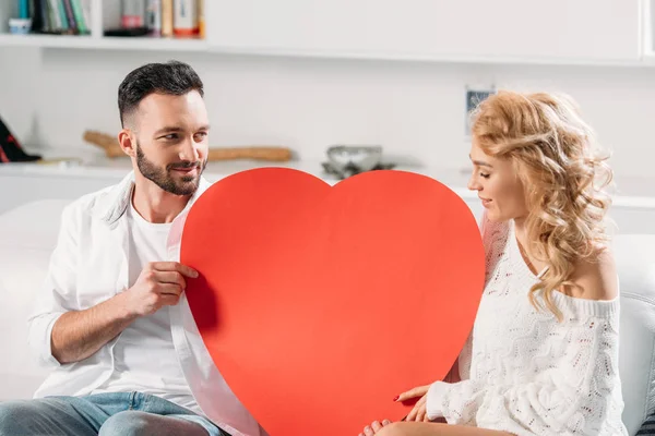 Romantic couple sitting on sofa with big red heart — Stock Photo