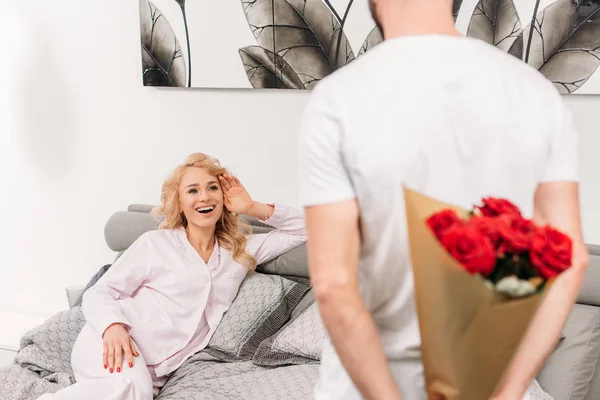 Cropped view of man hiding flowers for girlfriend — Stock Photo