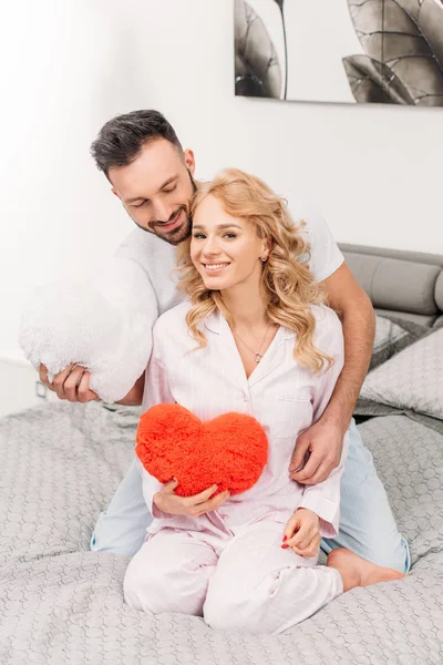 Feliz casal sentado na cama e segurando corações de brinquedo — Fotografia de Stock