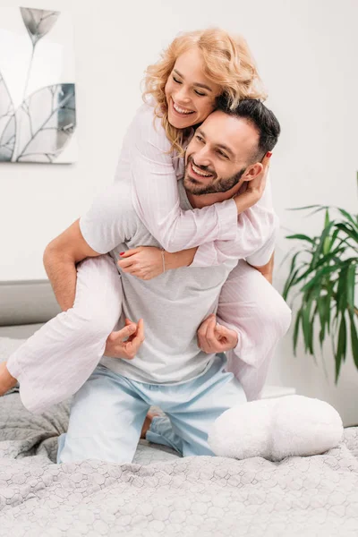 Ridendo donna romantica piggybacking fidanzato sul letto — Foto stock