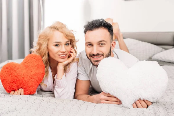 Усміхнена пара тримає іграшкові серця і лежить на ліжку — стокове фото