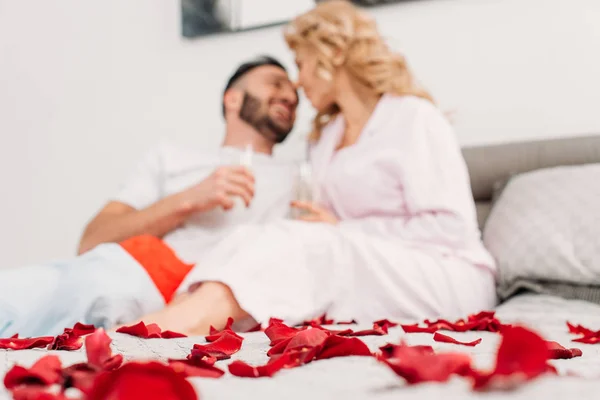 Casal rindo deitado na cama com taças de champanhe no dia dos namorados — Fotografia de Stock