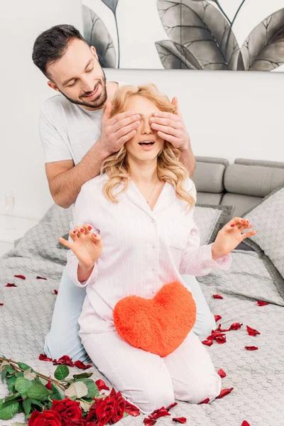 Man sitting on bed with roses and covering girlfriend's eyes — Stock Photo