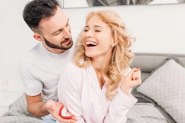 Brünetten Mann schlägt lachende Frau im Schlafzimmer vor — Stockfoto