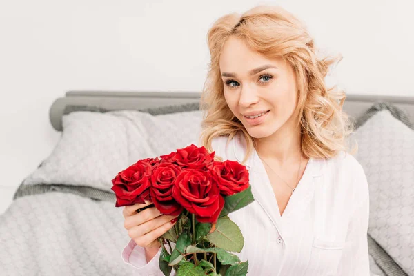 Fröhliches blondes Mädchen posiert mit Rosen im Schlafzimmer — Stockfoto