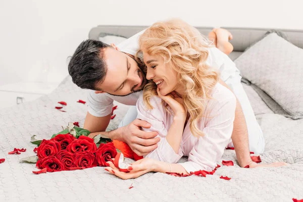 Pareja sonriente acostada en la cama con rosas y anillo - foto de stock