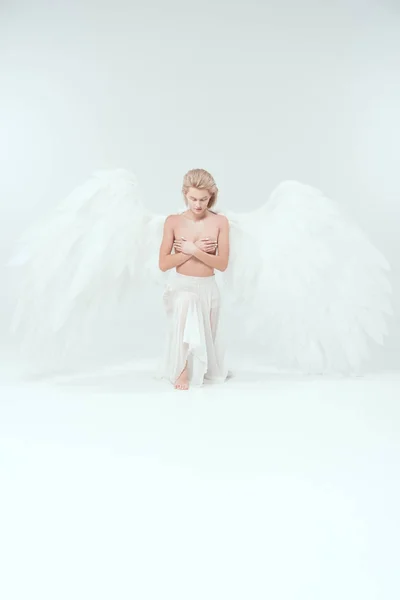 Beautiful tender woman with angel wings covering breasts while posing isolated on white — Stock Photo