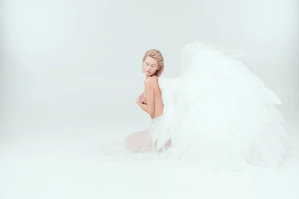 Schöne Frau mit Engelsflügeln sitzt und posiert isoliert auf weiß mit Kopierraum — Stockfoto