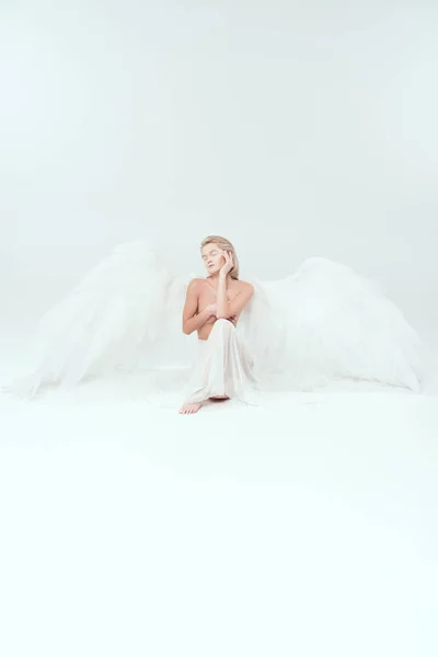 Beautiful woman with angel wings covering breasts and posing isolated on white with copy space — Stock Photo