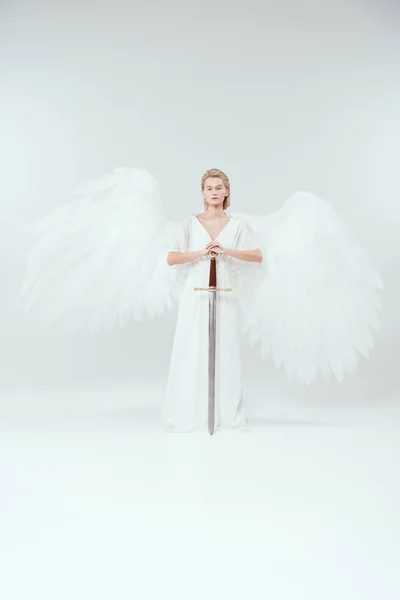 Beautiful woman with angel wings holding sword and posing on white background — Stock Photo